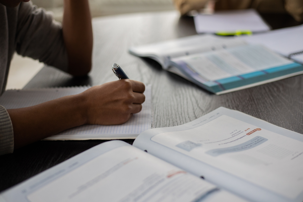 A person studying at a desk. Books and strewn about the desk and they are writing.